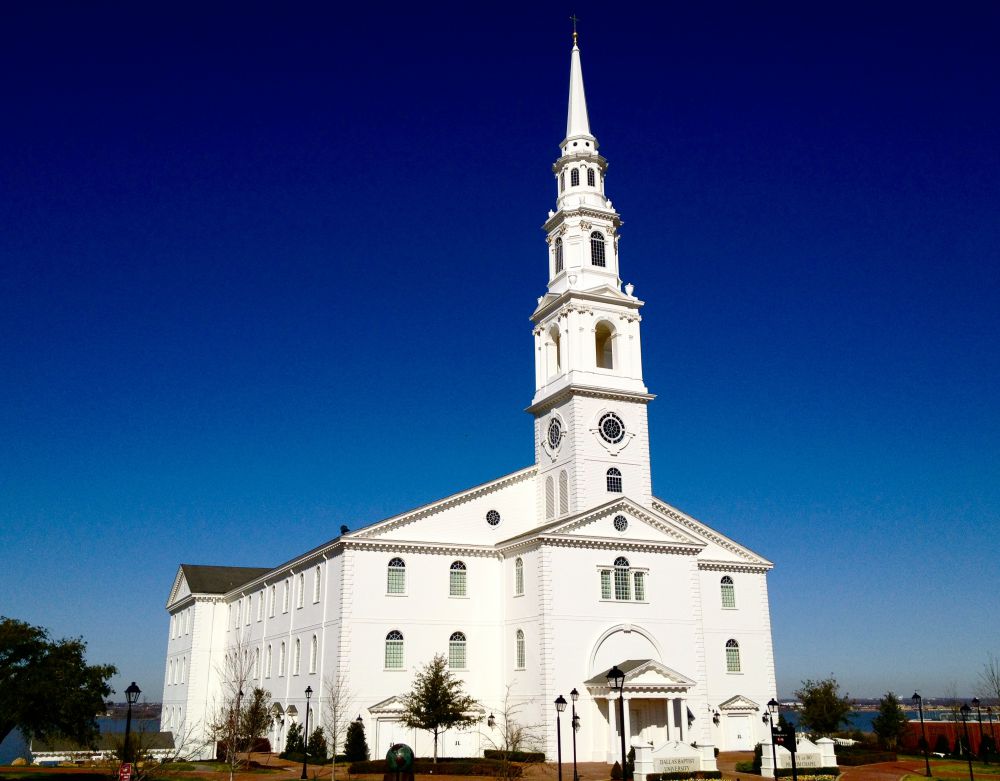 The white colonial Pilgrim Chapel and its tall steeple at Dallas Baptist University under a deep blue sky